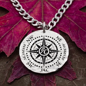 May include: Silver compass necklace with a black compass design and the initials "JC" in the center. The necklace has a silver chain and the compass has the words "NW", "NE", "SE", "SW", and "JAC" engraved on it.