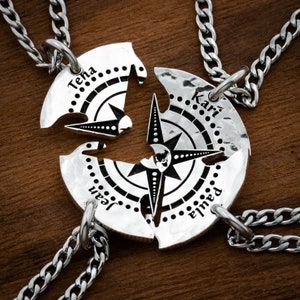 May include: Four silver necklaces with compass pendants that are split into four pieces. Each piece has a different name on it: Teha, Kari, Jean, and Elma.