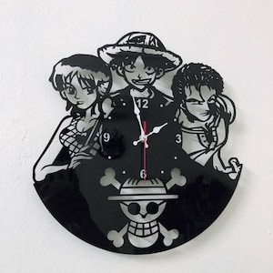 May include: Black wall clock featuring anime characters. The clock face has a circular design with a skull and crossbones emblem at the bottom. The clock hands are red and white.