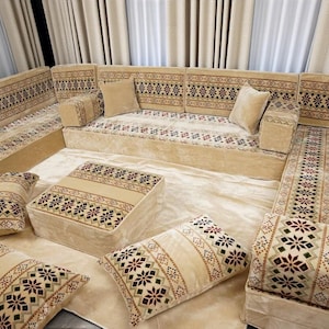 May include: Beige sectional sofa with patterned cushions and a matching ottoman. The sofa features a geometric design in red, green, and brown. The cushions and ottoman are arranged on a light beige rug.