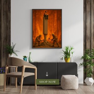 May include: Framed art print depicting a surreal scene. Two figures in firefighter gear use hammers to break the base of a pillar. A person sits atop the pillar, with a fiery forest backdrop. The art print is displayed above a black cabinet.