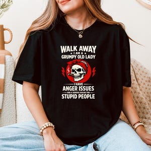 Könnte beinhalten: Schwarzes T-Shirt mit dem Text "WALK AWAY I AM A GRUMPY OLD LADY I HAVE ANGER ISSUES AND A SERIOUS DISLIKE FOR STUPID PEOPLE." Das Design zeigt einen Totenkopf mit rotem Bandana und Zigarre.