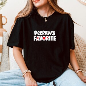 Könnte beinhalten: Schwarzes T-Shirt mit dem weißen Text "PeePaw's Favorite" und einem roten Herz. Das Shirt ist ein lässiger Stil, geeignet für den Alltag.
