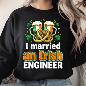 May include: Black sweatshirt with a St. Patrick's Day graphic. The design features two beer mugs with Irish flag colors, a pretzel, and the text "I married an Irish ENGINEER."