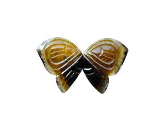 May include: A carved butterfly-shaped gemstone with a mix of brown, yellow, and black hues. The wings have detailed veining and a polished surface, creating a natural, elegant look. The gemstone is set against a white background.