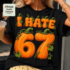 May include: A black t-shirt featuring a graphic print of orange pumpkins shaped into the letters of the words I HATE and the number 67. The design includes green vines and leaves wrapped around the pumpkin-shaped characters on the front.