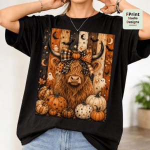 May include: A black t-shirt featuring a graphic of a brown Highland cow wearing a plaid bow, surrounded by pumpkins, ghosts, bats, and stars against a vertical striped background. The text FPrint Studio Designs appears in the top right corner.