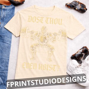 K&ouml;nnte beinhalten: Beigefarbenes T-Shirt mit goldfarbener Illustration eines Ritters beim Gewichtheben. Der Text "DOST THOU EVEN HOIST?" ist oberhalb und unterhalb des Ritters aufgedruckt. Sonnenbrille und wei&szlig;e Turnschuhe sind sichtbar.