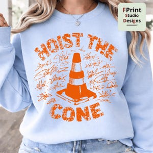 May include: Light blue sweatshirt with an orange graphic of a traffic cone and the words "HOIST THE CONE". The design includes stylized signatures around the cone. The sweatshirt is a crew neck style.