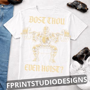 K&ouml;nnte beinhalten: Wei&szlig;es T-Shirt mit einer goldenen Illustration eines Ritters, der Gewichte hebt, mit dem Text "DOST THOU EVEN HOIST?" &uuml;ber und unter dem Bild. Das Shirt hat auch den Text "FPRINTSTUDIODESIGNS" unten.