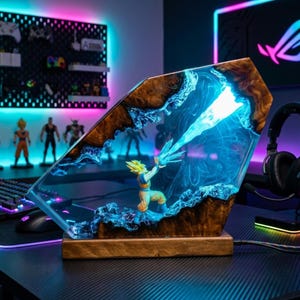 May include: A unique resin lamp featuring a detailed figurine of a character from Dragon Ball Z. The lamp has a wooden base and a clear resin body with blue accents, creating a vibrant, illuminated display. The lamp is designed with a distinctive, angular shape.