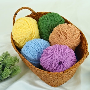 May include: A woven basket filled with six balls of colorful yarn. The yarn is in shades of yellow, green, peach, blue, and purple. The basket has a handle and is sitting on a white surface.
