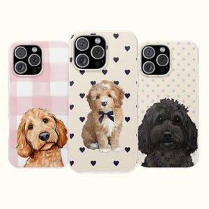Könnte beinhalten: Drei Smartphone-Hüllen mit Hundeillustrationen. Die linke Hülle hat ein rosa Karomuster und einen goldbraunen Hund. Die mittlere Hülle hat einen cremefarbenen Hintergrund mit marineblauen Herzen und einen braunen Hund mit Fliege. Die rechte Hülle hat blaue Punkte.