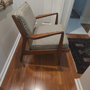 May include: Mid-century modern armchair with a wooden frame and houndstooth patterned upholstery. The chair has a low profile, angled legs, and armrests. The seat and back are covered in a black and white fabric.