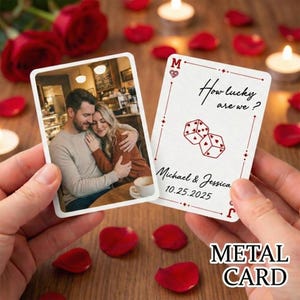 May include: Two metal cards are held in hands, one with a photo of a couple, the other with the text "How lucky are we?" and dice graphics. The cards are surrounded by rose petals and candles, with the text "Michael & Jessica 10.25.2025".
