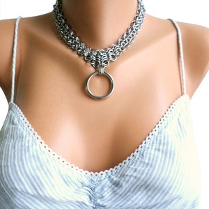 May include: A silver chainmail choker necklace with a large silver ring pendant.
