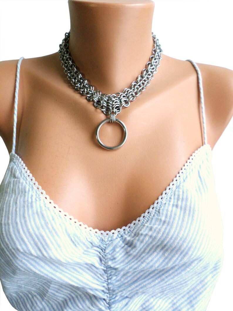 May include: A silver chainmail choker necklace with a large silver ring pendant.