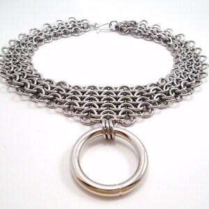 May include: A silver chainmail choker necklace with a large silver ring pendant.