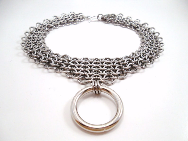 May include: A silver chainmail choker necklace with a large silver ring pendant.