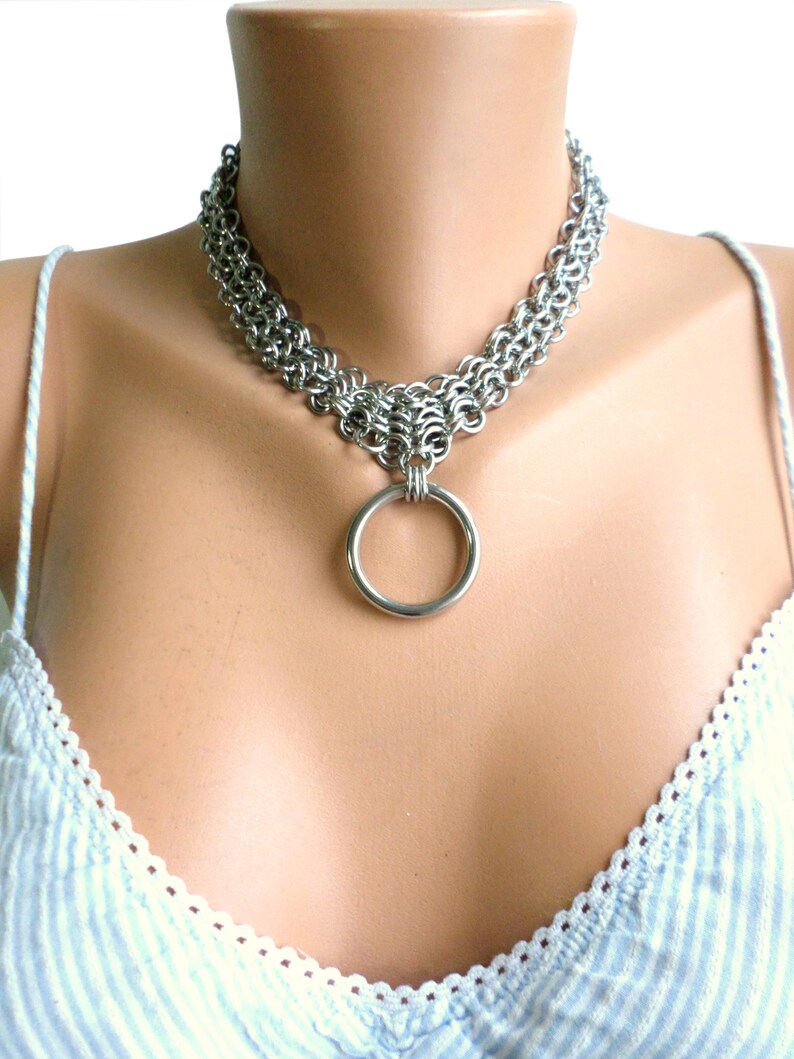 May include: A silver chainmail choker necklace with a large silver ring pendant.