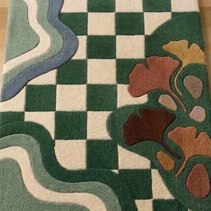 May include: A rectangular rug with a green and white checkerboard pattern, accented by a flowing design in shades of blue, green, and white. The rug also features a botanical design with brown and yellow leaf shapes.