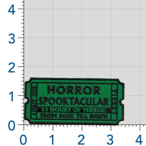 May include: A rectangular green embroidered patch shaped like a ticket, measuring approximately 3.5 inches wide and 1.5 inches tall. It features black text reading HORROR SPOOKTACULAR, 12 HOURS OF TERROR, FROM DUSK TILL DAWN, ADMIT ONE, and TICKET.