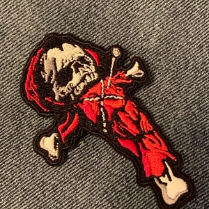 May include: Embroidered patch featuring a skeletal figure in red and white, with a black border. The design includes a skull, rib cage, and other anatomical details. The patch is likely for clothing or accessories.