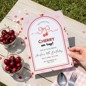 Op de afbeelding: Een roze verjaardagsuitnodiging met een kersenthema. De tekst luidt "CHERRY on top!" en nodigt gasten uit voor Amelia's 10e verjaardag. Twee kleine glazen kommen met kersen en confetti liggen op een houten tafel.