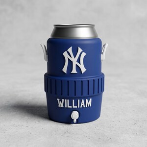 May include: A navy blue beverage cooler with a silver top and white handles. The cooler features the New York Yankees logo in white and the name "WILLIAM" in white lettering. It has a small spigot at the bottom.