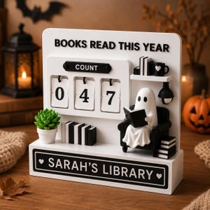 May include: A white wooden book tracker sign with the text BOOKS READ THIS YEAR and SARAH'S LIBRARY. It features a flip-style counter showing 047, a small potted succulent, stacks of black and white books, and a ghost figure reading in a chair.