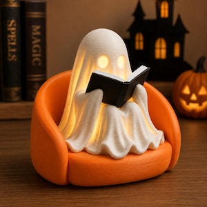 May include: A white, glowing ghost figurine sitting in a bright orange armchair. The ghost has two circular eye cutouts and is holding an open black book. The surface of the ghost and the chair features a fine, linear 3D-printed texture.