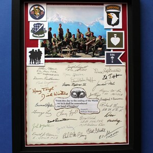 Puede incluir: Obra de arte enmarcada con una fotografía vintage de soldados, insignias militares y firmas. La imagen incluye el texto "Hang Tough" y una cita de Shakespeare. El marco es negro.