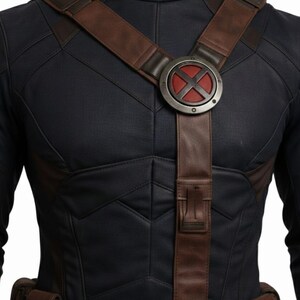 Pu&ograve; includere: Un costume blu navy con cinghie e cintura in pelle marrone. Il petto presenta un emblema circolare con un design a "X" rosso. Il costume ha un motivo trapuntato e due piccole tasche sulla cintura.