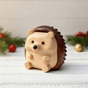 May include: A wooden hedgehog figurine with a light brown face and belly, dark brown back, and black eyes. The figurine has a slot on top and is sitting on a white wooden surface. Christmas decorations are in the background.