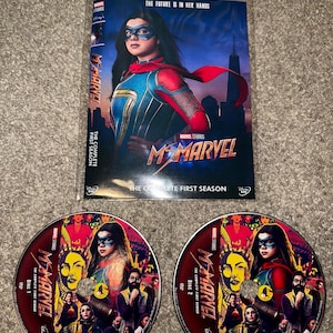 Może przedstawiać: Zestaw DVD serialu Marvel Studios, Ms. Marvel. Okładka przedstawia główną bohaterkę w kostiumie superbohatera. Dyski są czerwone z grafiką postaci. Tekst na okładce brzmi "The Complete First Season."