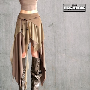 May include: A layered skirt in shades of brown and beige with an asymmetrical, draped design. The skirt is worn with a matching top and brown boots. The image includes the text "ESSENTIALS".