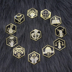 Puede incluir: Una colección de doce pines hexagonales de esmalte con bordes dorados y fondos negros. Cada pin muestra un símbolo gráfico blanco único, incluyendo una pata de oso, arco y flecha, un libro abierto, espadas, una balanza y varias manos.