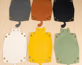 May include: Six flat, cat-shaped trays arranged in two rows. Each tray features a smooth surface in gray, brown, black, white, yellow, or sage green, with metallic rivets at the corners and edges, and a small tail-shaped extension at the bottom.