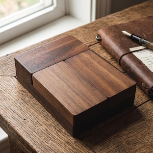 May include: A rectangular dark brown wooden box with a smooth finish and a lid composed of three distinct segments. The box features a visible wood grain pattern and a clean, geometric design with sharp edges, presenting a solid and sturdy appearance.