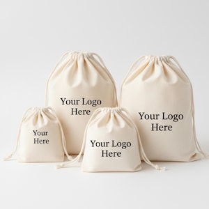 Op de afbeelding: Vier beige trekkoordzakken van verschillende maten tegen een witte achtergrond. Elke tas heeft de tekst "Your Logo Here" of "Your Here" erop. De tassen zijn gemaakt van een zachte, natuurlijke stof.