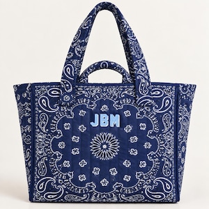 May include: A quilted tote bag in deep navy blue featuring a white paisley pattern throughout. The bag has two top handles and a smaller secondary handle. Centered on the front is the light blue embroidered monogram text JBM in block letters.