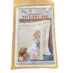May include: A packaged children's pillowcase kit. The pillowcase features a cross-stitch design of teddy bears, flowers, and bows. The packaging includes the text "CHILDREN'S PILLOWCASE" and "SLEEPING FRIENDS".