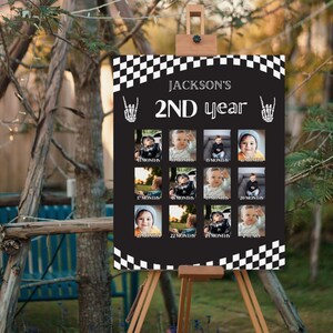 Pode incluir: Uma placa preta em um cavalete, exibindo uma grade de fotos de bebês. A placa diz "2º ano de Jackson" com as fotos do bebê rotuladas com meses. As bordas superior e inferior têm um design de bandeira quadriculada.