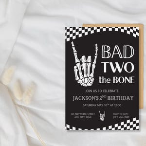 May include: A black and white rectangular birthday invitation card featuring a checkered border, a skeleton hand making a rock-and-roll gesture, and the text BAD TWO the BONE, JOIN US TO CELEBRATE JACKSON'S 2ND BIRTHDAY, SATURDAY MAY 10TH AT 12:00.