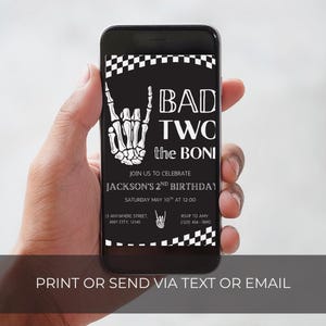 May include: A black smartphone displaying a digital birthday invitation with a white skeleton hand making a rock-and-roll gesture, a checkered border, and the text BAD TWO the BONE, JOIN US TO CELEBRATE JACKSON'S 2ND BIRTHDAY, SATURDAY MAY 10TH AT 12:00.