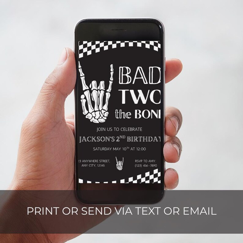 May include: A black smartphone displaying a digital birthday invitation with a white skeleton hand making a rock-and-roll gesture, a checkered border, and the text BAD TWO the BONE, JOIN US TO CELEBRATE JACKSON'S 2ND BIRTHDAY, SATURDAY MAY 10TH AT 12:00.