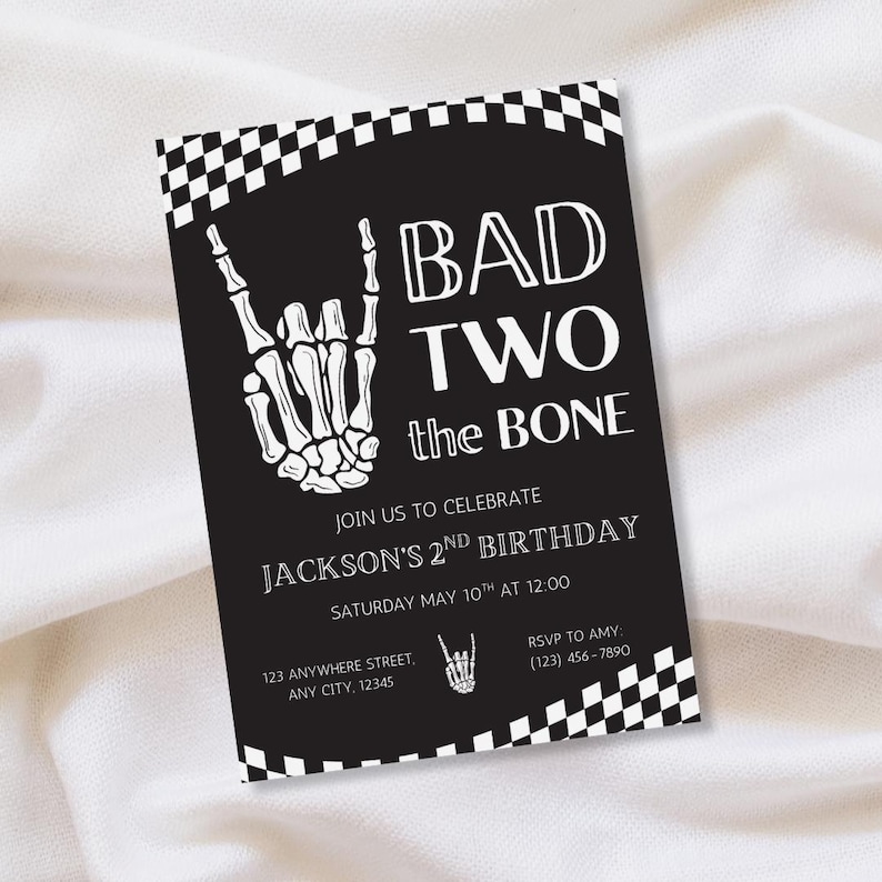 May include: A black rectangular birthday invitation card featuring a white skeleton hand making a rock-and-roll gesture, a checkered border, and the text BAD TWO the BONE, JOIN US TO CELEBRATE JACKSON'S 2ND BIRTHDAY, SATURDAY MAY 10TH AT 12:00.