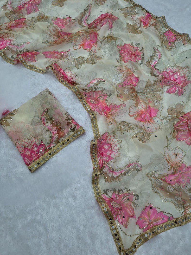 May include: A cream-coloured fabric with a floral pattern in pink and brown hues. The fabric features sequins and a gold border. A matching square piece of fabric is also visible.