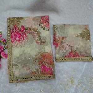 May include: A sheer fabric set with a floral pattern, comprising a large rectangular piece and a smaller square piece. The design features pink and brown floral motifs on a cream background, with a gold mirrored border.