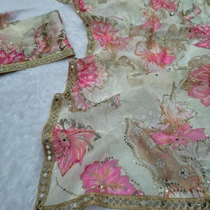 May include: A delicate fabric featuring a floral design in pink and beige hues. It has a gold border with small reflective sequins. The image shows a matching piece, possibly a scarf or accessory, complementing the main fabric.